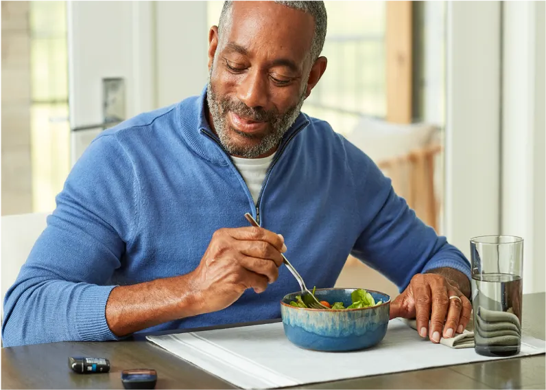 Elderly man eating a bowl of salad at a dining table.