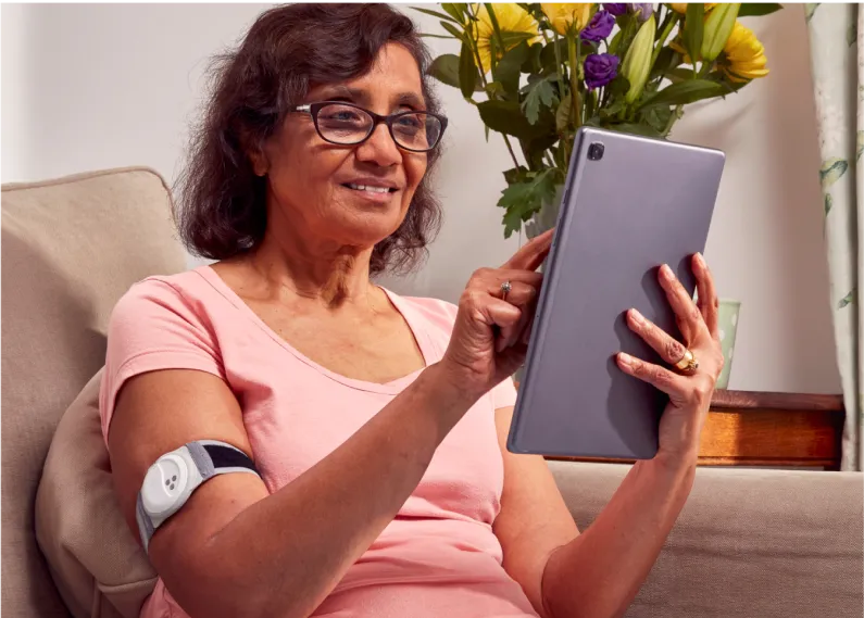 Elderly lady operating a tablet device with a monitoring device around her arm.