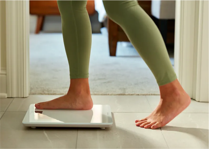 Person stepping on a white weight scale.