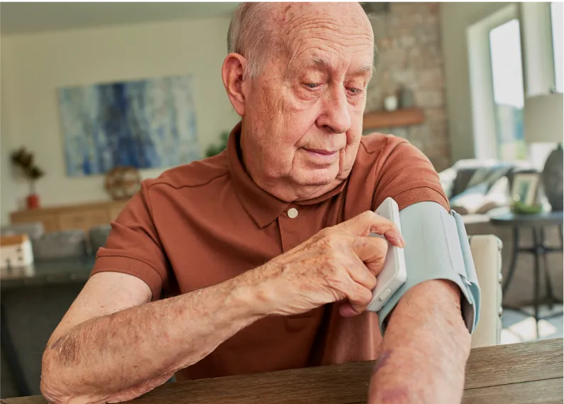 Elderly man operating monitoring device wrapped around his arm.